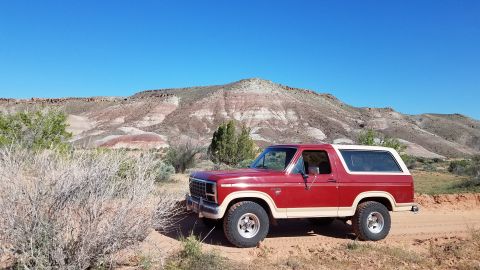 1985 Ford Bronco - This two-tone 1985 Ford Bronco is captured in a scenic desert location, with mountains forming a backdrop.