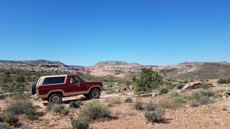 Red and tan Ford Bronco parked on a dirt road in a desert landscape
