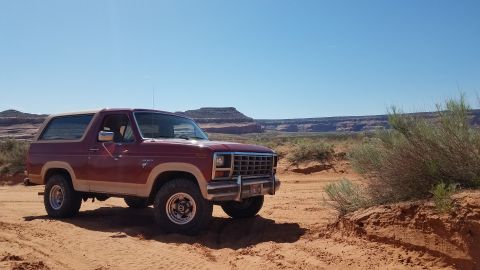 1985 Ford Bronco - This 1985 Ford Bronco is seen in a desert landscape with red rock formations visible in the distance.