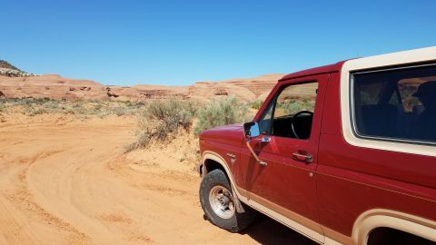 1985 Ford Bronco - This classic Ford Bronco is parked on a dusty trail with arid desert scenery under a clear blue sky.