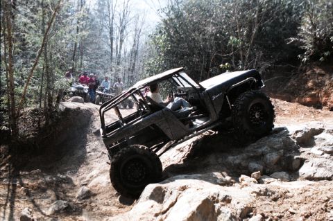 1976 Ford Bronco - A 1976 Ford Bronco navigates a rocky off-road course, while spectators watch from ATVs on a nearby ridge.