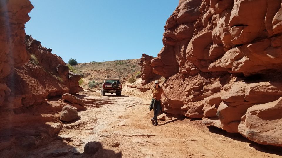 Red Ford Bronco driving on a dirt road through a canyon, spare tire mounted on the rear door