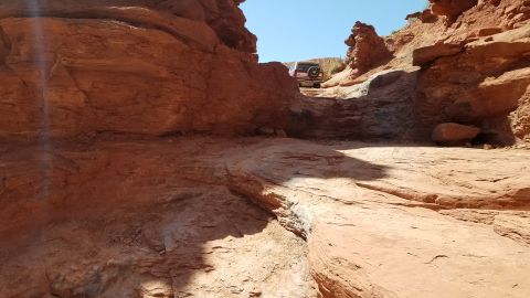 1985 Ford Bronco - An SUV navigates a challenging off-road path through a canyon with red rock formations.