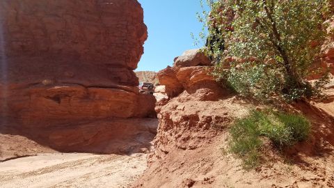 1985 Ford Bronco - Off-road vehicles navigate a tight passage between towering red rock formations under a clear blue sky.