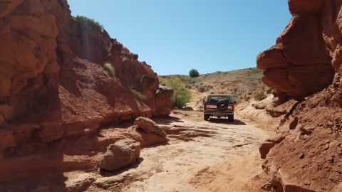 1985 Ford Bronco - A red 1985 Ford Bronco navigates a dusty trail through a canyon under a clear blue sky.