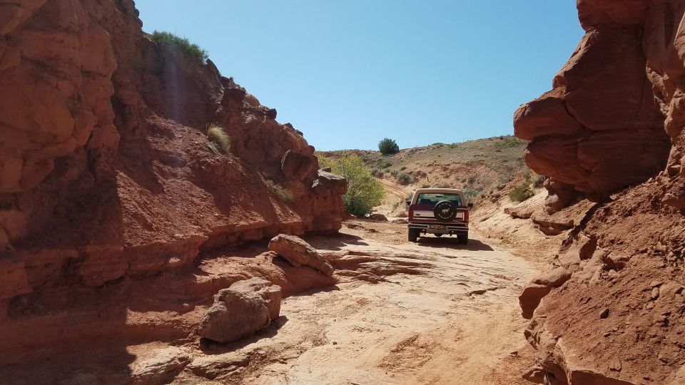Red 1985 Ford Bronco driving on a rocky desert road