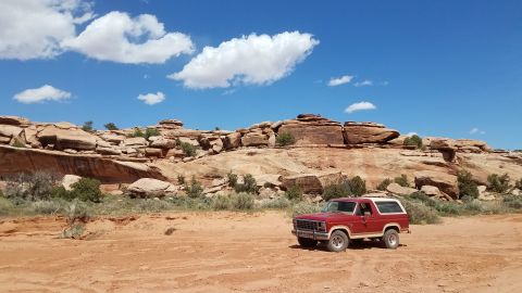 1985 Ford Bronco - 1985 Ford Bronco parked in a desert landscape with red rock formations under a blue sky.