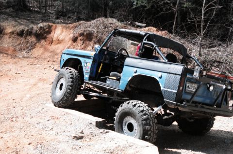 1976 Ford Bronco - Modified 1976 Ford Bronco navigates a challenging off-road terrain, dirt trail with a lifted suspension and large, aggressive tires.
