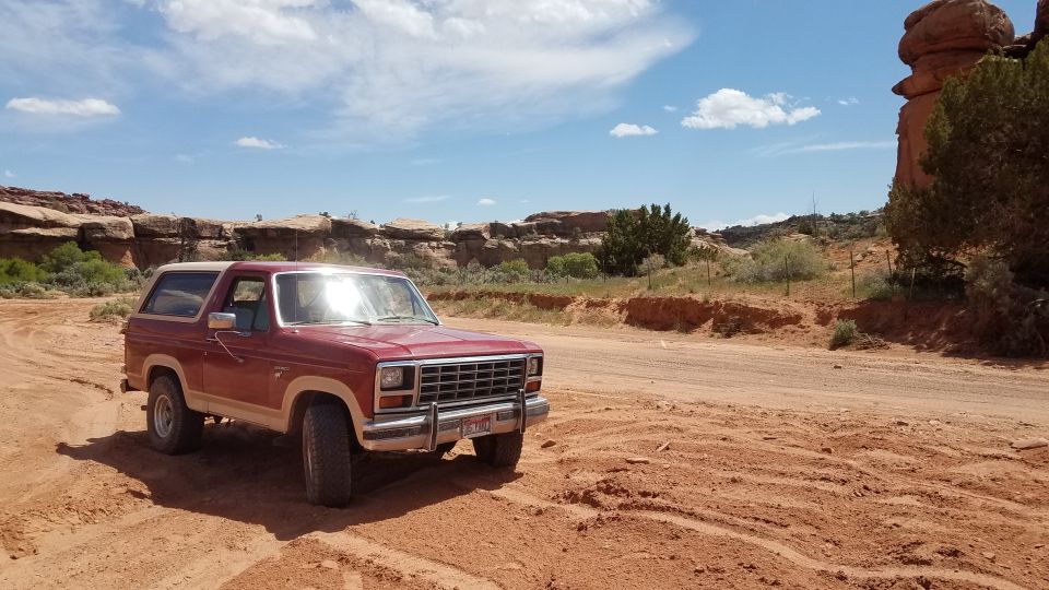 Red Ford Bronco parked on a dirt road with rocky cliffs in the background