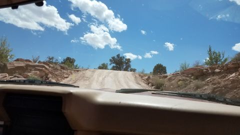 1985 Ford Bronco - Driving through a rocky, desert landscape on a sunny day with a clear blue sky and scattered clouds.