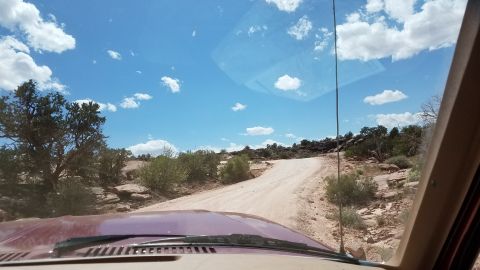 1985 Ford Bronco - Driving on a dirt road in a desert environment. The sky is blue with scattered clouds.