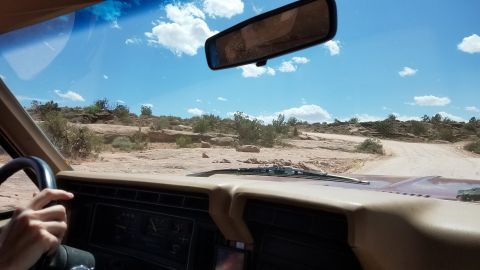 1985 Ford Bronco - Driving through a rocky, arid landscape under a bright blue sky with scattered clouds.