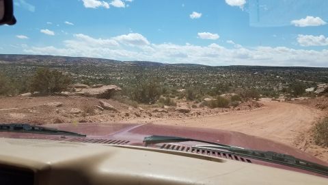 1985 Ford Bronco - View from inside a vehicle driving on a dirt road through a vast, arid landscape under a partly cloudy sky.