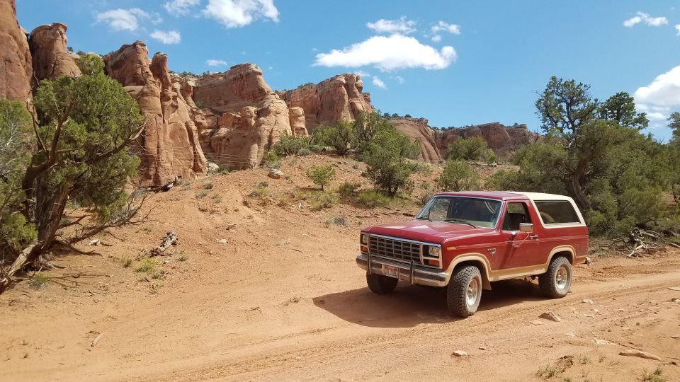Red Ford Bronco parked on a dirt road in a desert landscape with red rock formations