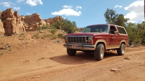 1985 Ford Bronco - This 1980s Ford Bronco is parked on a dusty trail with desert scenery and a bright blue sky.