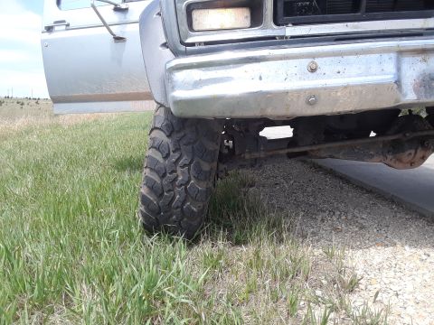 1985 Ford Bronco - Close-up of a truck's front corner, showing a large tire and part of the bumper and door.