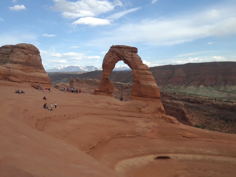 Delicate Arch, a natural sandstone arch, with people gathered around and mountains in the background