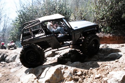 1976 Ford Bronco - This heavily modified off-road vehicle navigates a rocky trail, with ATVs in the background.