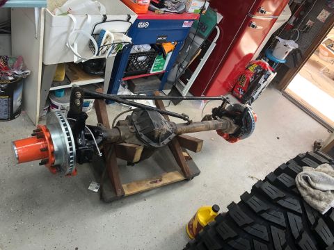 1992 Jeep Wrangler - A disassembled front axle assembly sits on wooden supports, with a large tire in the foreground.