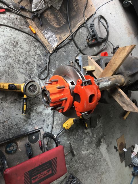 1992 Jeep Wrangler - A vehicle axle assembly with bright orange brake components sits on a workshop floor surrounded by tools and power equipment.
