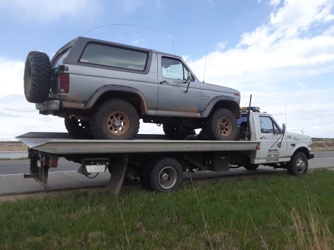 1985 Ford Bronco - A gray Ford Bronco is transported on a flatbed tow truck under a cloudy sky.