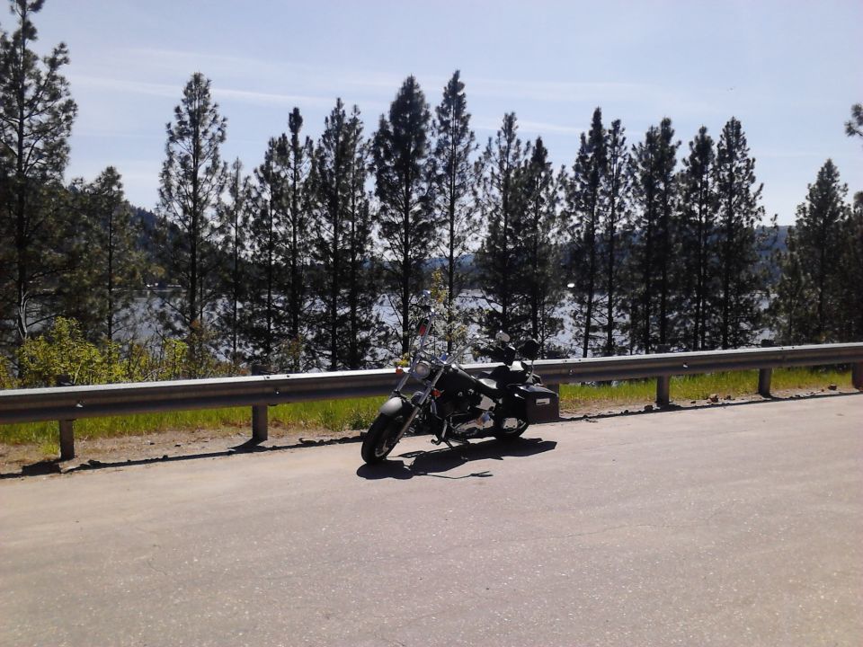 Motorcycle parked on roadside with lake and trees in background