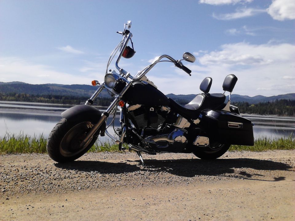 Black motorcycle parked on a gravel road next to a lake with mountains in the background