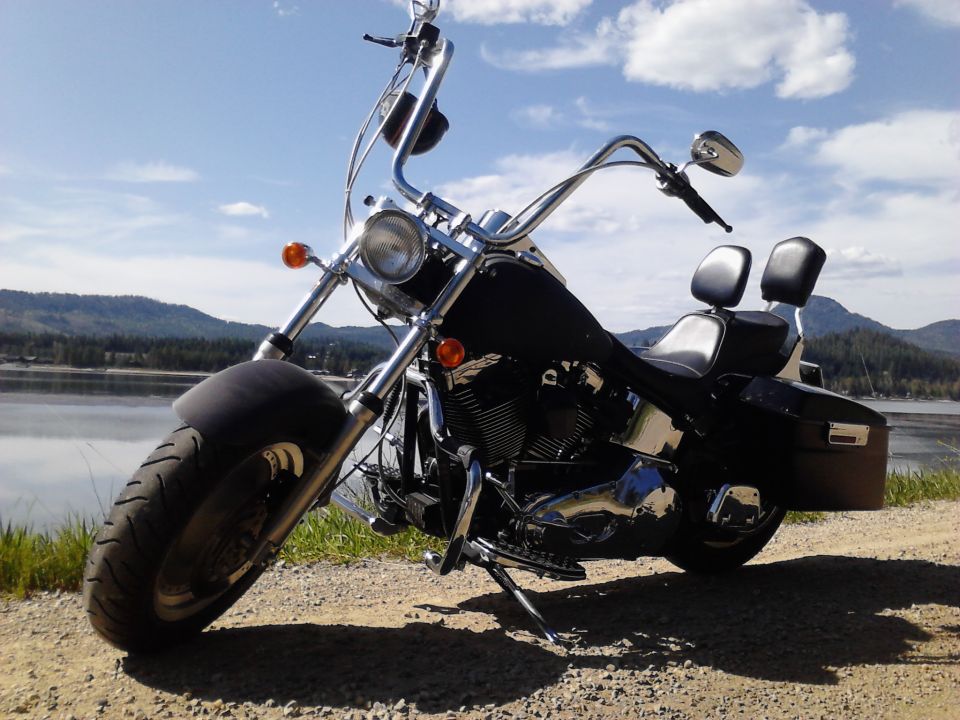 Black motorcycle with chrome handlebars and dual seats parked by a lake