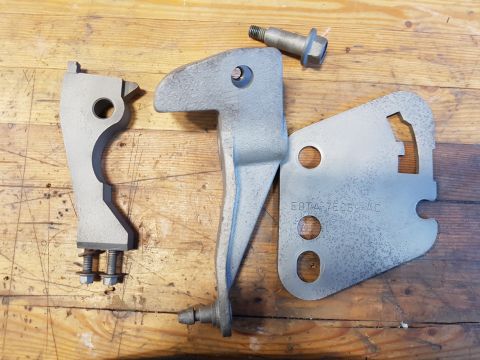 1978 Ford Bronco - Metal brackets and bolts are laid out on a wooden surface. One bracket has the part number E8TA-76069-AC stamped on it.