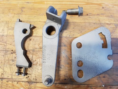 1978 Ford Bronco - Metal vehicle components shown on a wooden workbench. Part numbers are visible on two pieces.