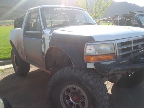 1985 Ford Bronco - This modified Ford Bronco features off-road tires and a custom roll cage, with another vehicle in the background.
