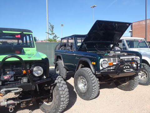 1985 Ford Bronco - Multiple off-road vehicles are parked outdoors under a clear blue sky.