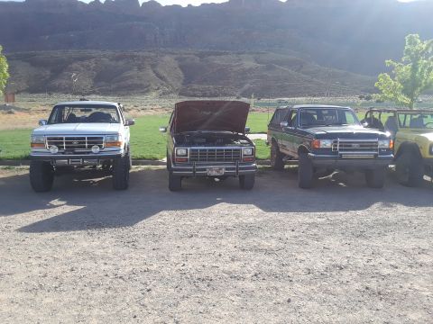 1985 Ford Bronco - Three SUVs are parked outdoors with a mountainous landscape behind them.