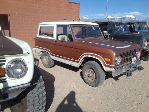 1985 Ford Bronco - A brown Ford Bronco with a white top is parked in a lot with other vehicles visible.