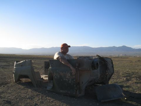 1981 Ford Bronco - A man sits in the remains of a vehicle in a barren landscape under a clear blue sky.