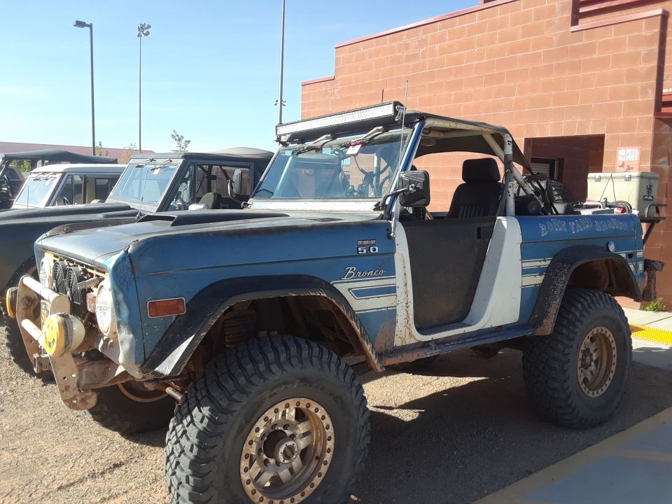 Blue Ford Bronco with off-road tires and a light bar on top. Another Bronco is parked behind it