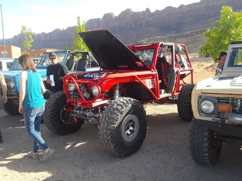 1985 Ford Bronco - Modified red off-road vehicle and a tan Ford Bronco parked outdoors with rocky hills in the background.