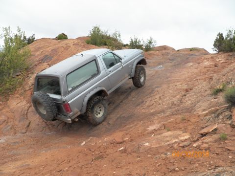 1985 Ford Bronco - A silver Ford Bronco navigates a challenging off-road course with steep inclines and rocky terrain.