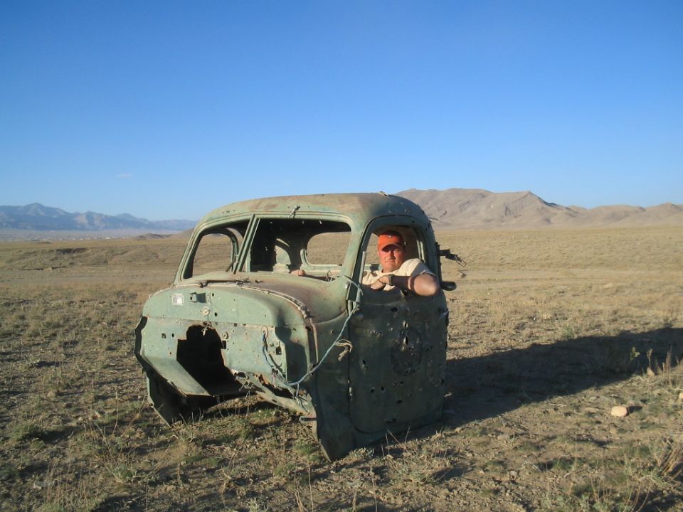 Bullet-riddled abandoned vintage pickup cab in desert with man sitting inside