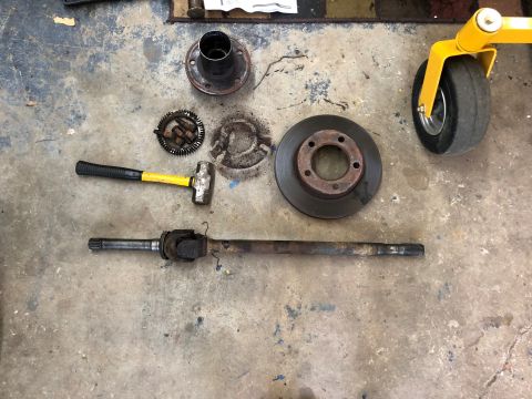 1995 Ford Bronco - Disassembled brake and drive axle components laid out on a concrete surface with a yellow and black sledgehammer.