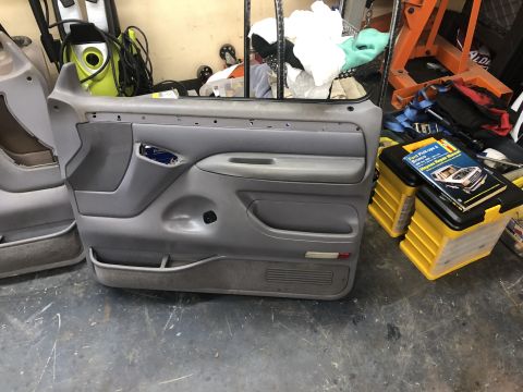 1995 Ford Bronco - Two gray car door panels are shown in a cluttered garage setting, with a repair manual visible.