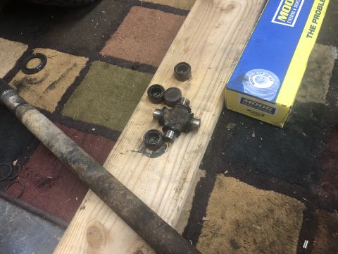 1995 Ford Bronco - A driveshaft part and a new u-joint are laid out on a wooden plank, with a box of Moog parts nearby.