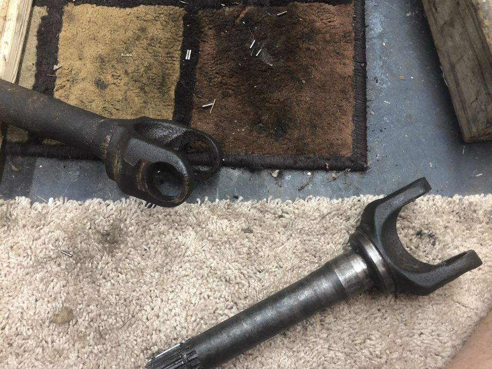 Two driveshaft yokes on a carpeted floor, one with a U-joint attached