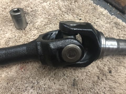 1995 Ford Bronco - A close-up view of a driveshaft universal joint, possibly for a Ford Bronco, resting on a carpeted surface next to a socket.