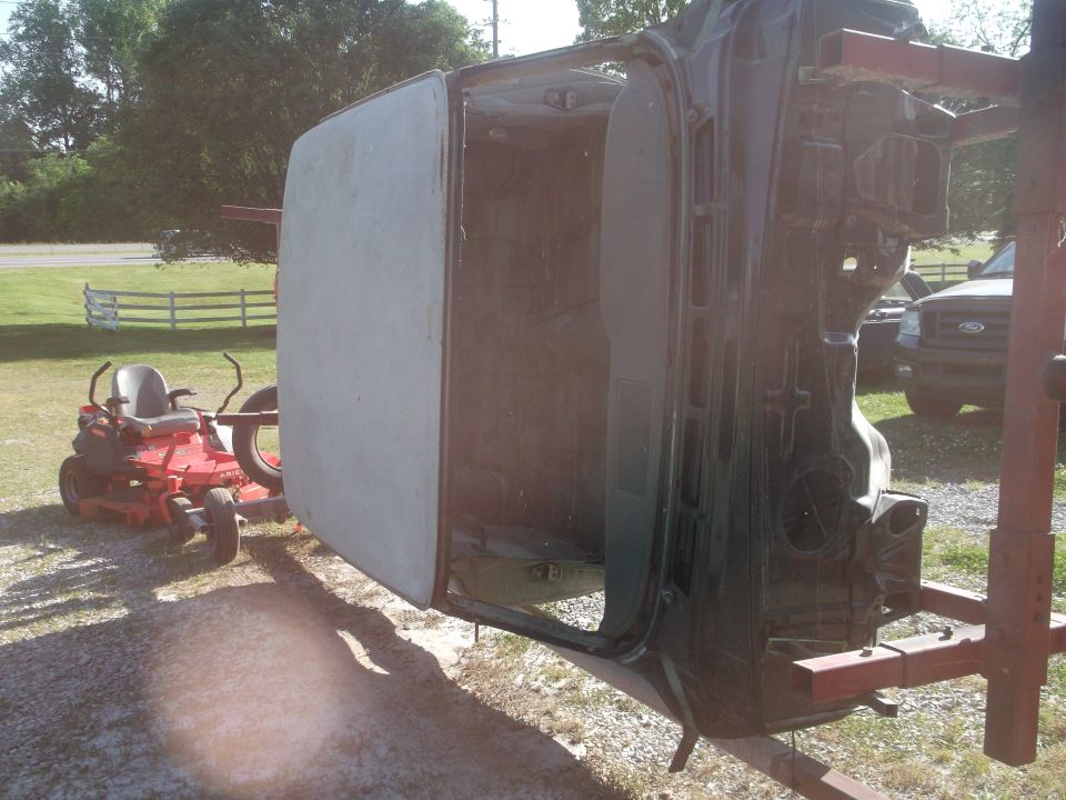Car body upside down on a rotisserie, with a lawn tractor nearby. Another vehicle is visible in the background