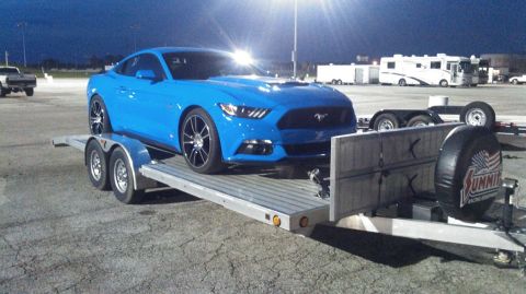 2017 Ford Mustang - A blue Ford Mustang is transported on a trailer at dusk, with other vehicles and RVs in the background.