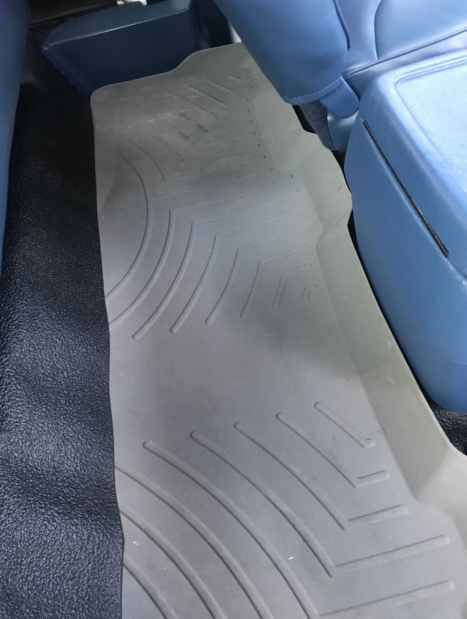 Gray rubber floor mat on black carpet with blue vinyl seats and center console