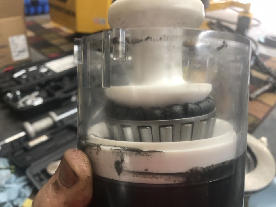 Close-up of a bearing inside a clear plastic housing, with a hand holding it. Tools are visible in the background