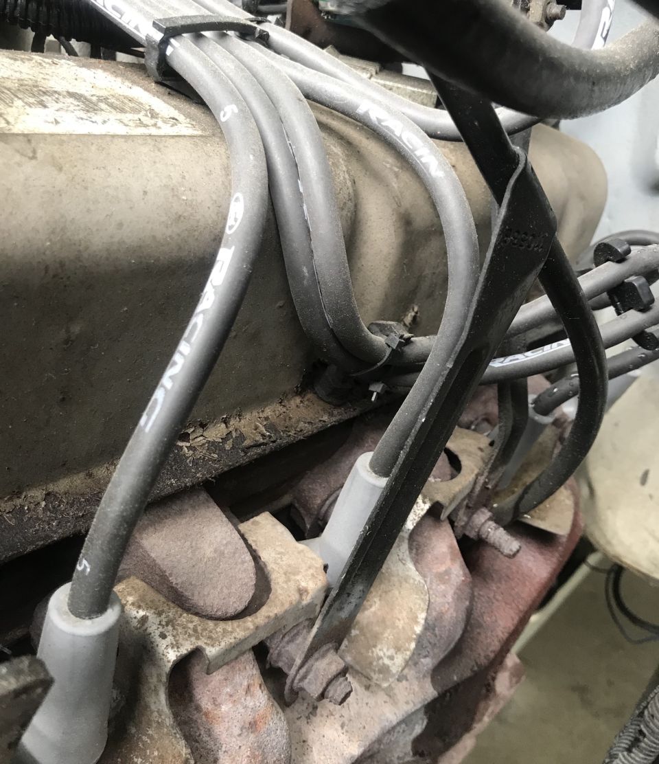 Engine spark plug wires on a dirty engine block with visible rust