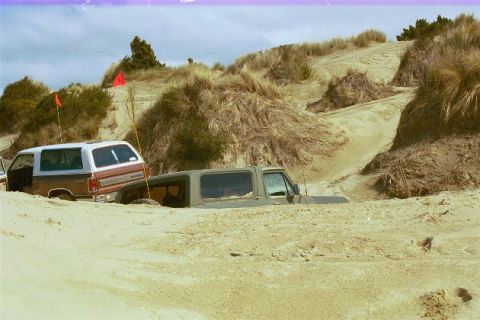 1979 Ford Bronco - Two SUVs are stuck in the sand dunes, with one vehicle almost completely buried.